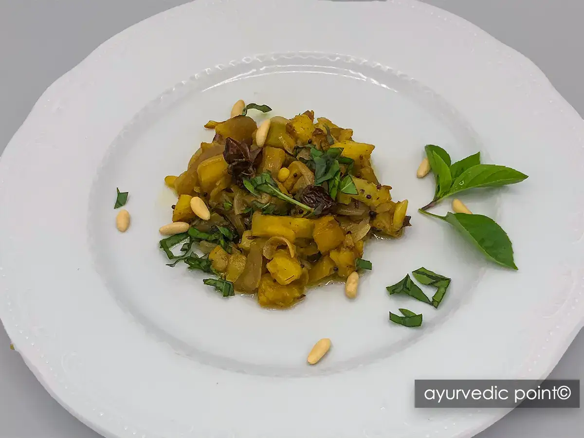 Melanzane speziate con pinoli, olive taggiasche e basilico fresco su piatto bianco - ricetta ayurvedica
