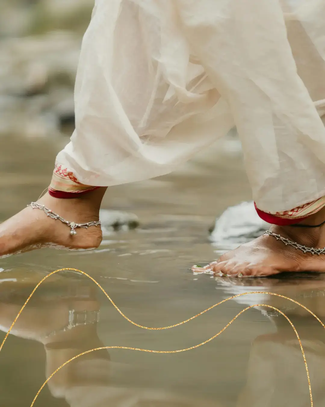 Piedi adornati con cavigliere mentre camminano scalzi nell’acqua, immagine evocativa del valore simbolico e rituale del piede nella cultura indiana