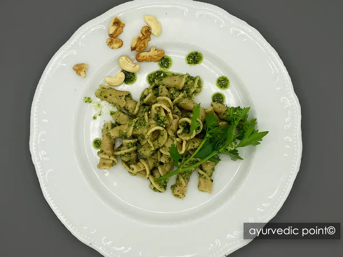 Piatto di pasta corta con pesto di foglie di sedano, noci e anacardi, guarnito con foglie fresche di sedano – Ayurvedic Point